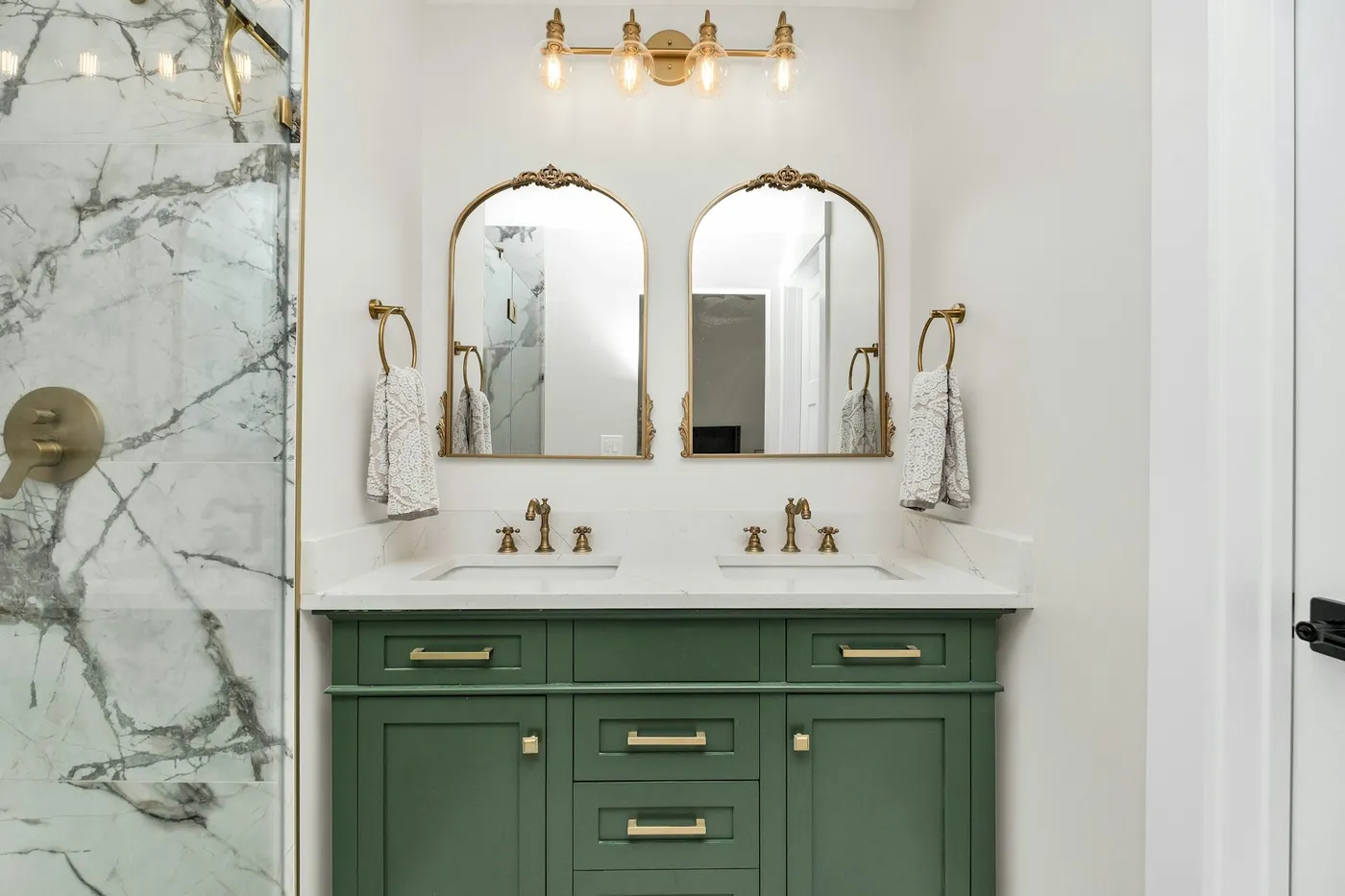 Bathroom with green double vanity, arched brass mirrors and marble shower